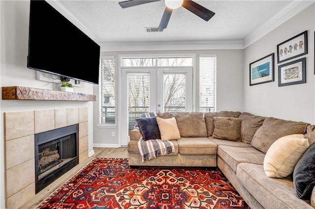 living room with hardwood / wood-style flooring, ornamental molding, a textured ceiling, a tiled fireplace, and french doors