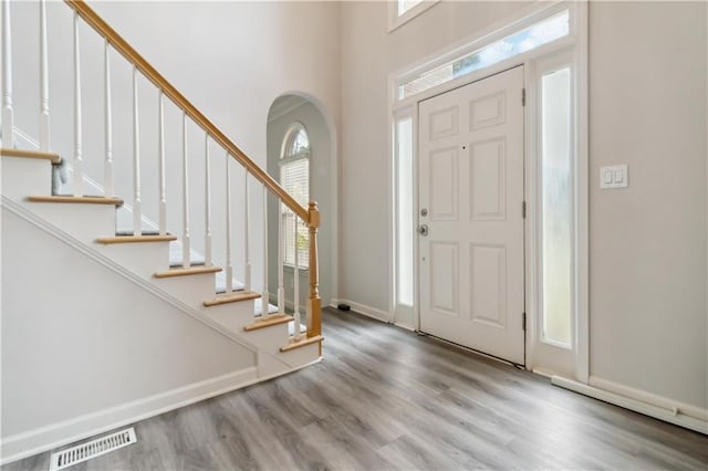 foyer with visible vents, wood finished floors, stairway, arched walkways, and baseboards