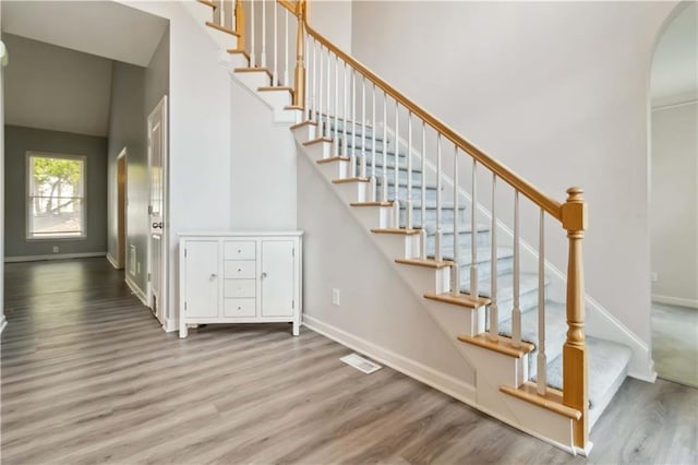 staircase featuring arched walkways, visible vents, baseboards, and wood finished floors