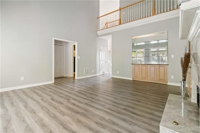 unfurnished living room featuring visible vents, a towering ceiling, baseboards, and wood finished floors