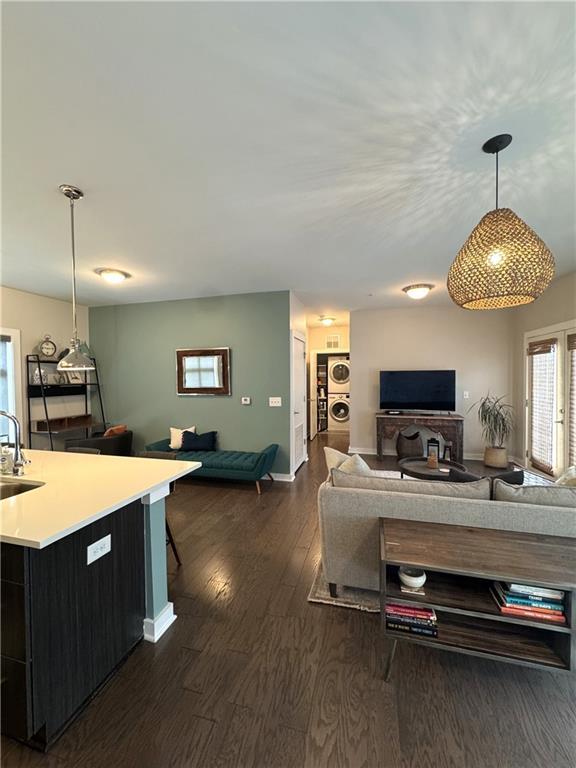 living room with dark wood-type flooring, baseboards, and stacked washer and dryer