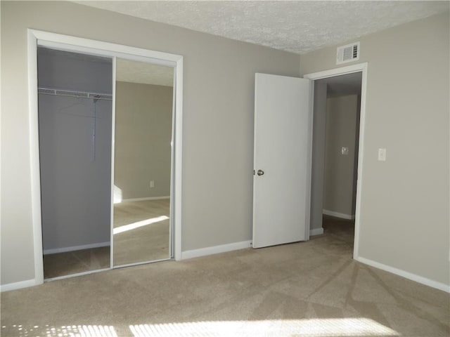 unfurnished bedroom featuring light carpet, a closet, and a textured ceiling