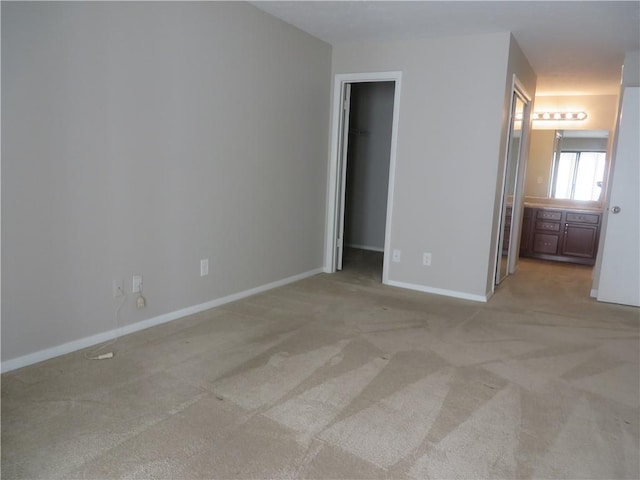 unfurnished bedroom featuring connected bathroom, a walk in closet, a closet, and light colored carpet