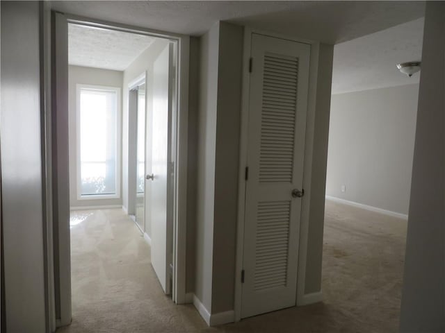 hallway with light colored carpet and a textured ceiling