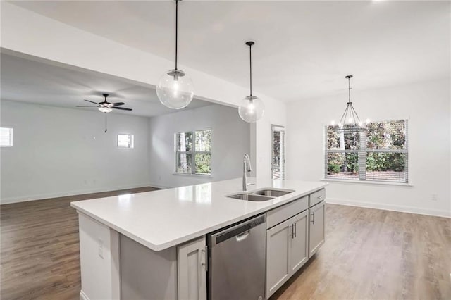 kitchen featuring light wood-type flooring, sink, dishwasher, hanging light fixtures, and an island with sink