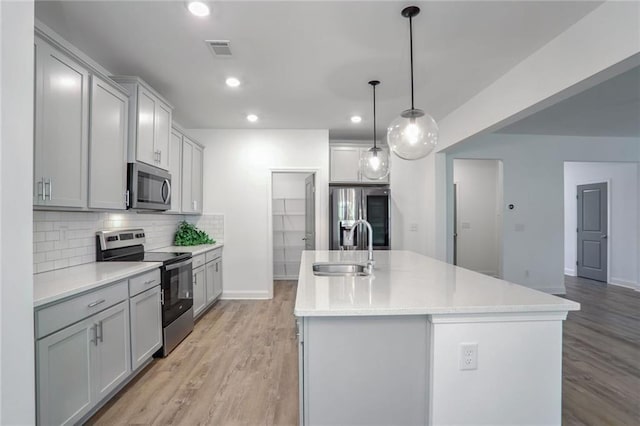 kitchen with a center island with sink, sink, hanging light fixtures, light hardwood / wood-style flooring, and stainless steel appliances