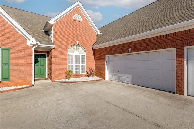 view of front of property featuring a garage, roof with shingles, concrete driveway, and brick siding