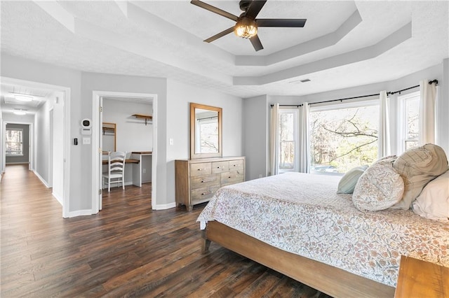 bedroom with ceiling fan, dark hardwood / wood-style flooring, and a tray ceiling