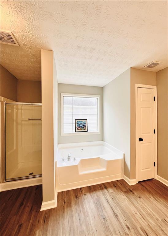 bathroom featuring independent shower and bath, wood-type flooring, and a textured ceiling