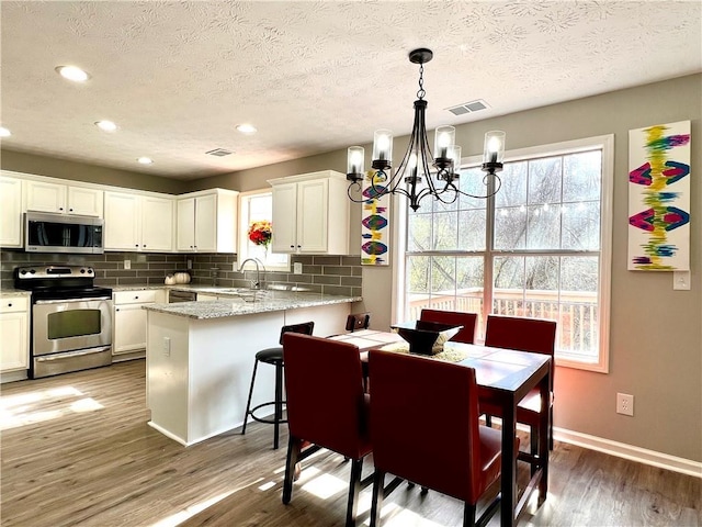 kitchen featuring dark wood-type flooring, white cabinetry, appliances with stainless steel finishes, kitchen peninsula, and a notable chandelier