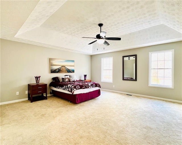 bedroom with ceiling fan, a raised ceiling, light carpet, and a textured ceiling