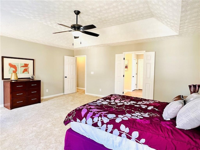 bedroom with light carpet, a tray ceiling, a textured ceiling, and ceiling fan