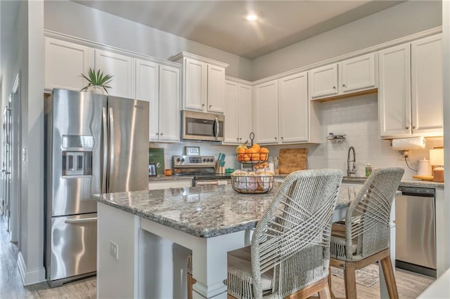 kitchen featuring decorative backsplash, light stone countertops, appliances with stainless steel finishes, and white cabinetry