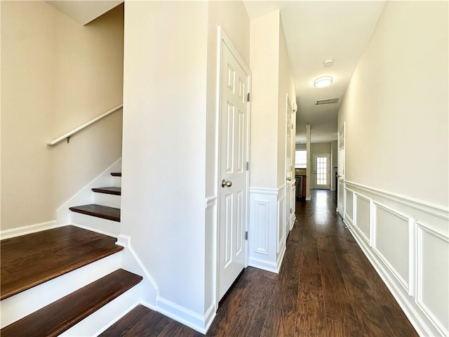 hallway featuring a decorative wall, dark wood-style flooring, visible vents, stairs, and wainscoting