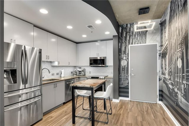 kitchen with backsplash, white cabinets, sink, appliances with stainless steel finishes, and light hardwood / wood-style floors