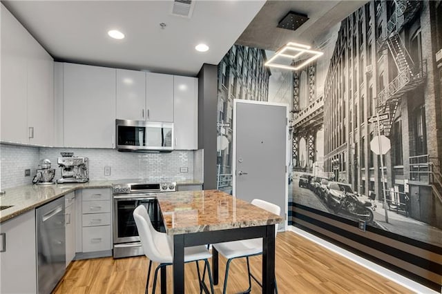 kitchen featuring white cabinets, light hardwood / wood-style flooring, tasteful backsplash, light stone counters, and stainless steel appliances