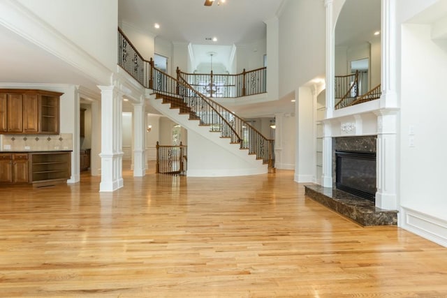 1565 Briergate Dr, Duluth, GA 30097 - unfurnished living room featuring light wood finished floors, a towering ceiling, stairway, crown molding, and a premium fireplace