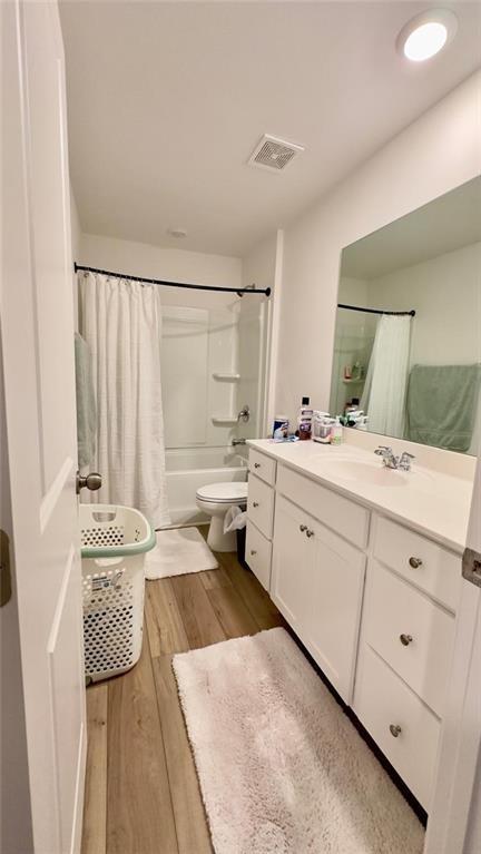 full bathroom featuring hardwood / wood-style floors, vanity, shower / bath combination with curtain, and toilet