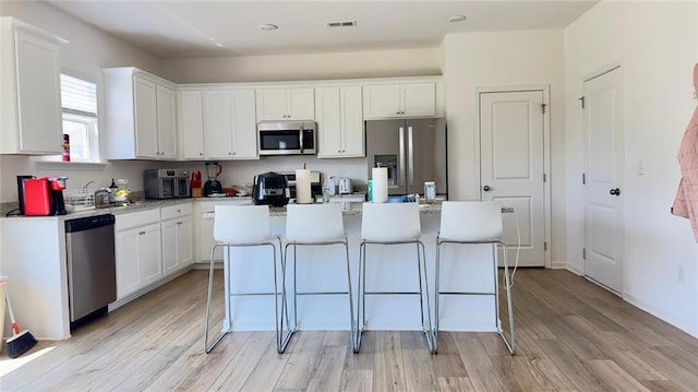 kitchen featuring stainless steel appliances, a kitchen island, white cabinetry, and light hardwood / wood-style floors