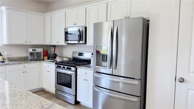 kitchen with light stone countertops, stainless steel appliances, white cabinetry, and light hardwood / wood-style flooring