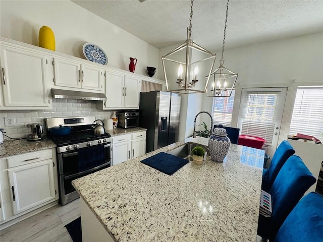 kitchen featuring stainless steel appliances, a kitchen island with sink, white cabinets, and decorative light fixtures