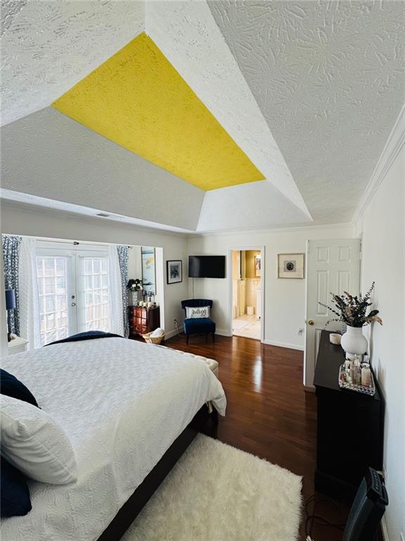 bedroom with a textured ceiling, a raised ceiling, hardwood / wood-style flooring, ensuite bathroom, and crown molding