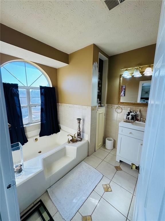 bathroom featuring tile walls, tile patterned floors, a bathing tub, and a textured ceiling