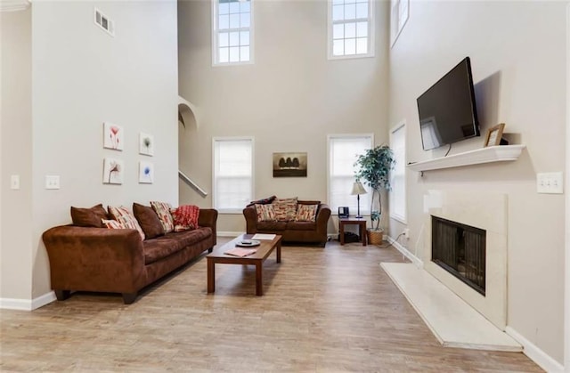living room with visible vents, light wood-type flooring, a high ceiling, and a high end fireplace