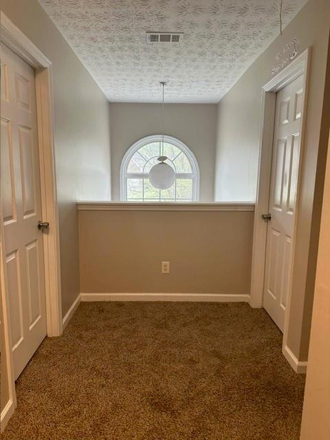 unfurnished dining area with a textured ceiling, visible vents, baseboards, and carpet