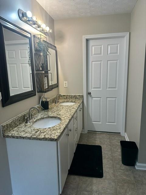full bath with a sink, tile patterned floors, double vanity, and a textured ceiling