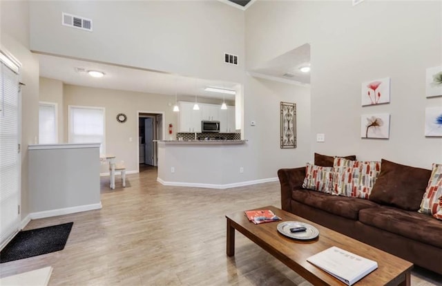 living area with a towering ceiling, visible vents, baseboards, and light wood finished floors