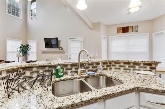 kitchen featuring white cabinets, a towering ceiling, a sink, and light stone counters