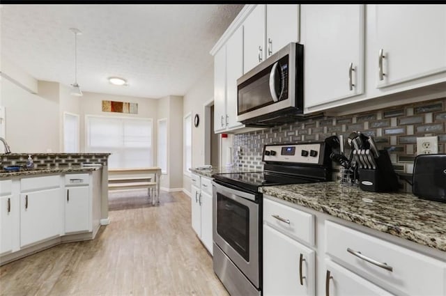 kitchen with light wood-style floors, a textured ceiling, white cabinets, appliances with stainless steel finishes, and backsplash