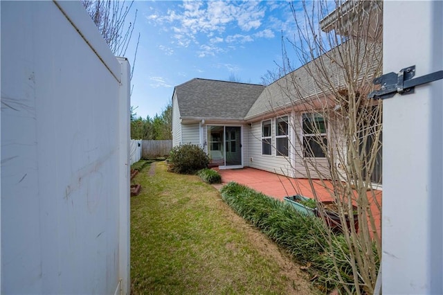 rear view of house featuring a shingled roof, fence, a lawn, and a patio