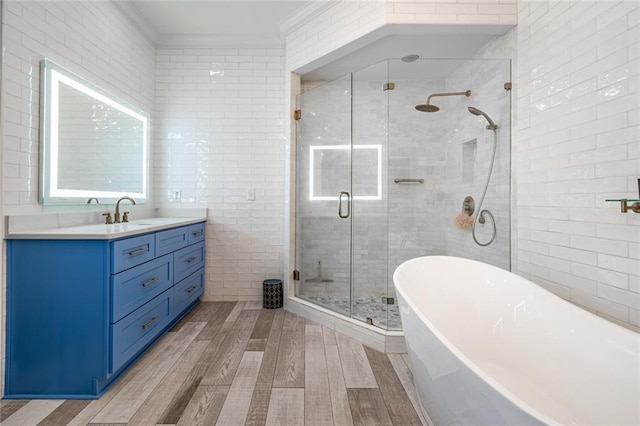 bathroom featuring vanity, wood finished floors, ornamental molding, a shower stall, and tile walls