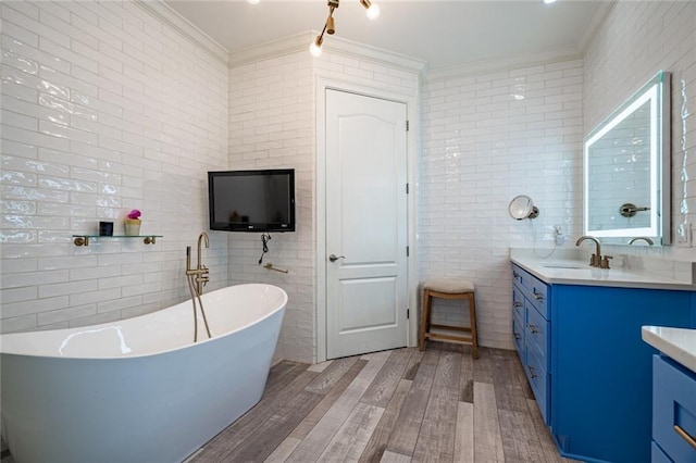 full bath featuring crown molding, wood finished floors, vanity, a freestanding tub, and tile walls