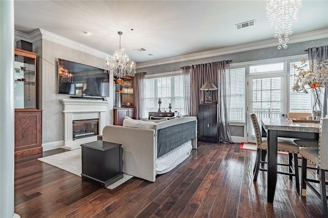 living area with visible vents, a fireplace with raised hearth, crown molding, dark wood-type flooring, and a chandelier