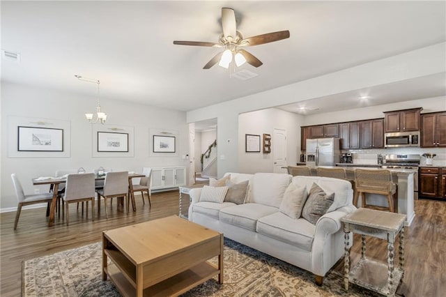 living room with ceiling fan with notable chandelier and dark hardwood / wood-style flooring