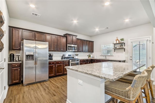 kitchen with a breakfast bar area, stainless steel appliances, light stone countertops, light hardwood / wood-style floors, and a kitchen island