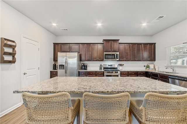 kitchen featuring light stone countertops, stainless steel appliances, a breakfast bar, and a center island