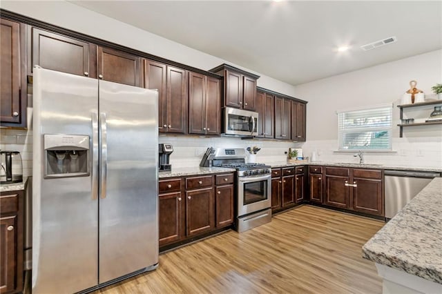 kitchen with sink, light hardwood / wood-style floors, stainless steel appliances, light stone countertops, and tasteful backsplash