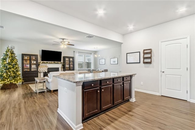 kitchen featuring a center island, light hardwood / wood-style flooring, dark brown cabinets, light stone counters, and ceiling fan with notable chandelier