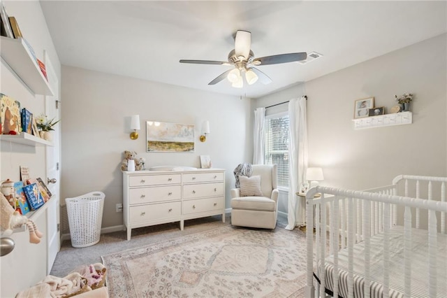 carpeted bedroom featuring ceiling fan and a nursery area