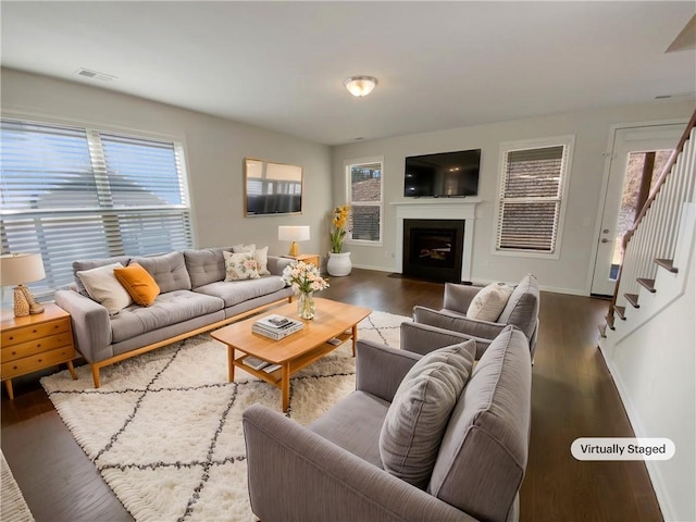 living room featuring stairway, a fireplace with flush hearth, wood finished floors, and visible vents