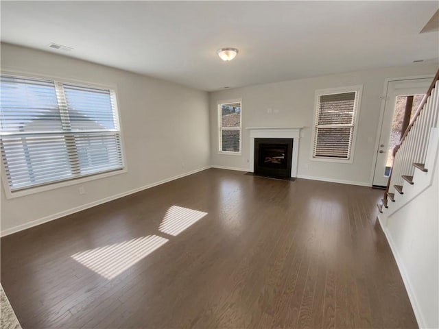 unfurnished living room featuring visible vents, plenty of natural light, dark wood-type flooring, and stairway