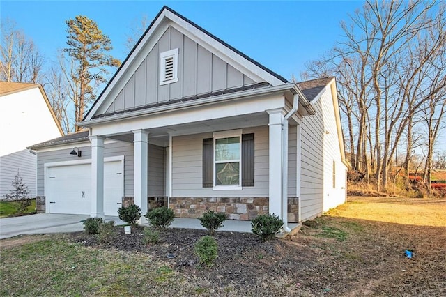 view of front of property featuring driveway, covered porch, a garage, stone siding, and board and batten siding