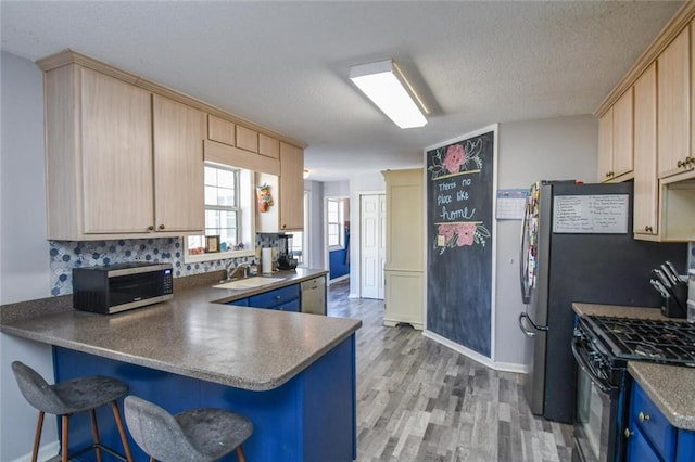 kitchen with stainless steel appliances, a sink, blue cabinets, light wood-style flooring, and a peninsula