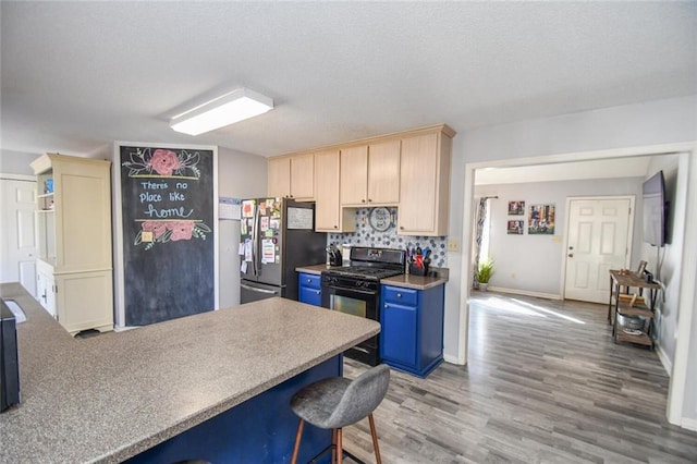 kitchen with freestanding refrigerator, black gas stove, blue cabinets, light wood finished floors, and light brown cabinetry