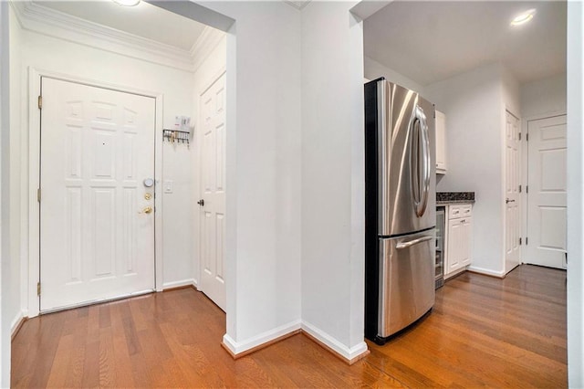 kitchen with stainless steel refrigerator, hardwood / wood-style floors, white cabinets, and ornamental molding