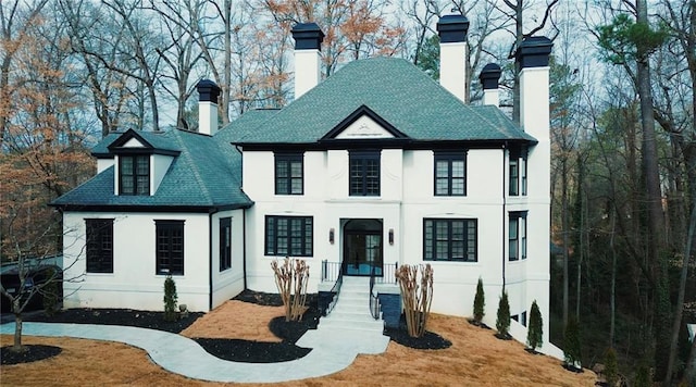 view of front of property featuring a shingled roof, french doors, a chimney, and stucco siding